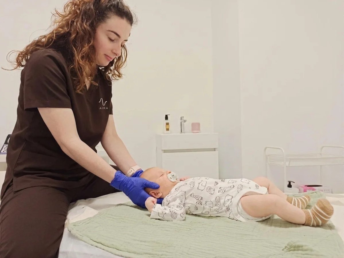 Fisioterapeuta atendiendo a un bebé tumbado en la camilla durante la primera visita de fisioterapia pediátrica