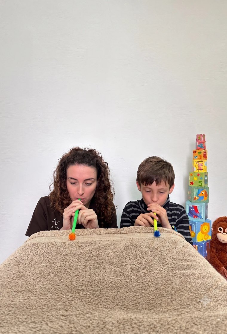 Fisioterapeuta y niño soplando un matasuegras en una sesión de fisioterapia respiratoria infantil en AIRA