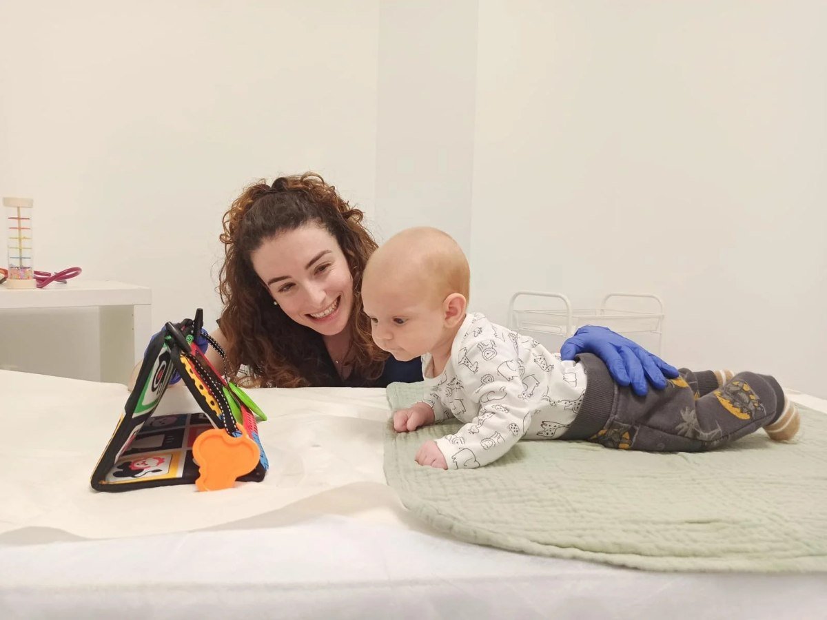 Fisioterapeuta jugando con un bebé boca abajo durante una sesión de fisioterapia pediátrica en AIRA